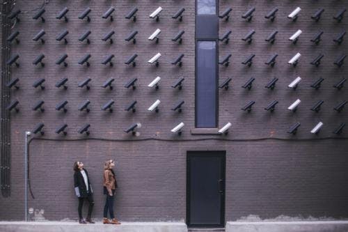 To mennesker som står ved en vegg som er dekket med kameraer
